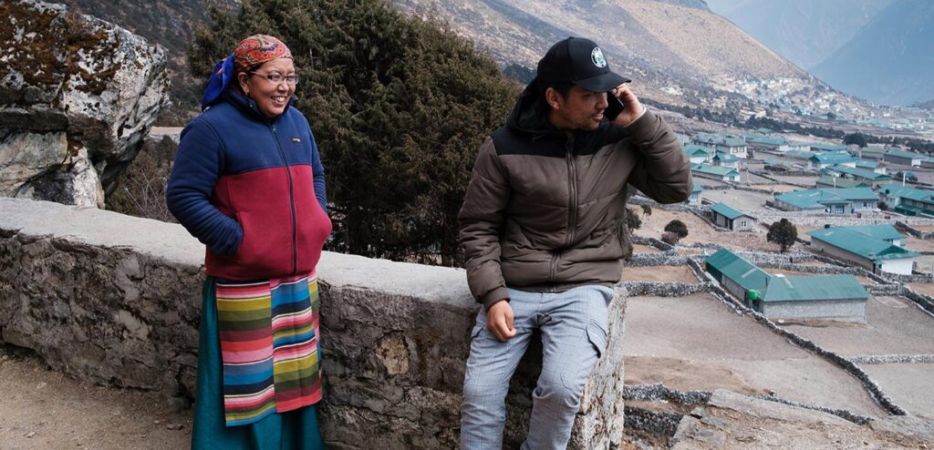 A man talking on the phone and a woman standing net to him and smiling