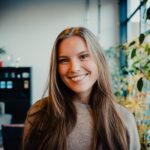 A woman with a warm smile stands in an office